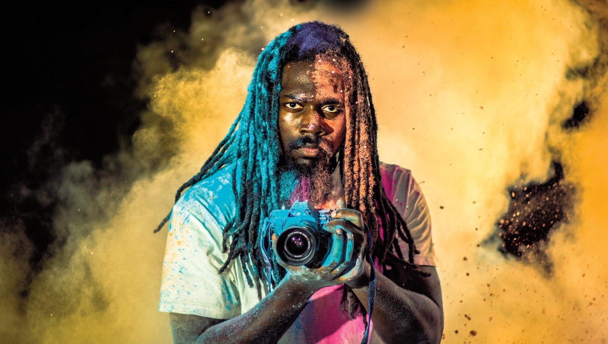A photographer holds his camera in the midst of a cloud of colorful smoke or dust